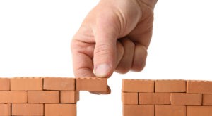 Picture of hand adding brick to a gap in the wall isolated on a white background