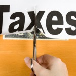 Picture of scissors cutting a piece of paper with taxes written on it.