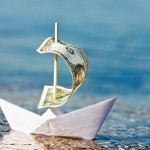 Picture of paper boat floating in water with dollar bill for sail.