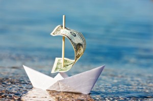 Picture of paper boat floating in water with dollar bill for sail.
