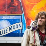 Picture of man standing in front of sign advertising Blue Moon brand beer