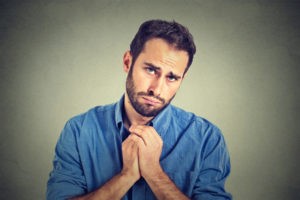Closeup portrait of desperate young man showing clasped hands, pretty please with sugar on top isolated on gray wall background. Human emotion facial expression feelings, body language