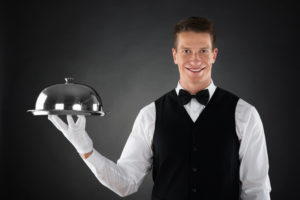 Portrait Of Happy Butler Holding Stainless Steel Cloche Over Tray