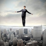 A man balances on a tight rope over a city skyline.