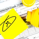 Form 1040 pictured with a bottle of Bayer aspirin and a doodle of a frowning face on a sticky note.